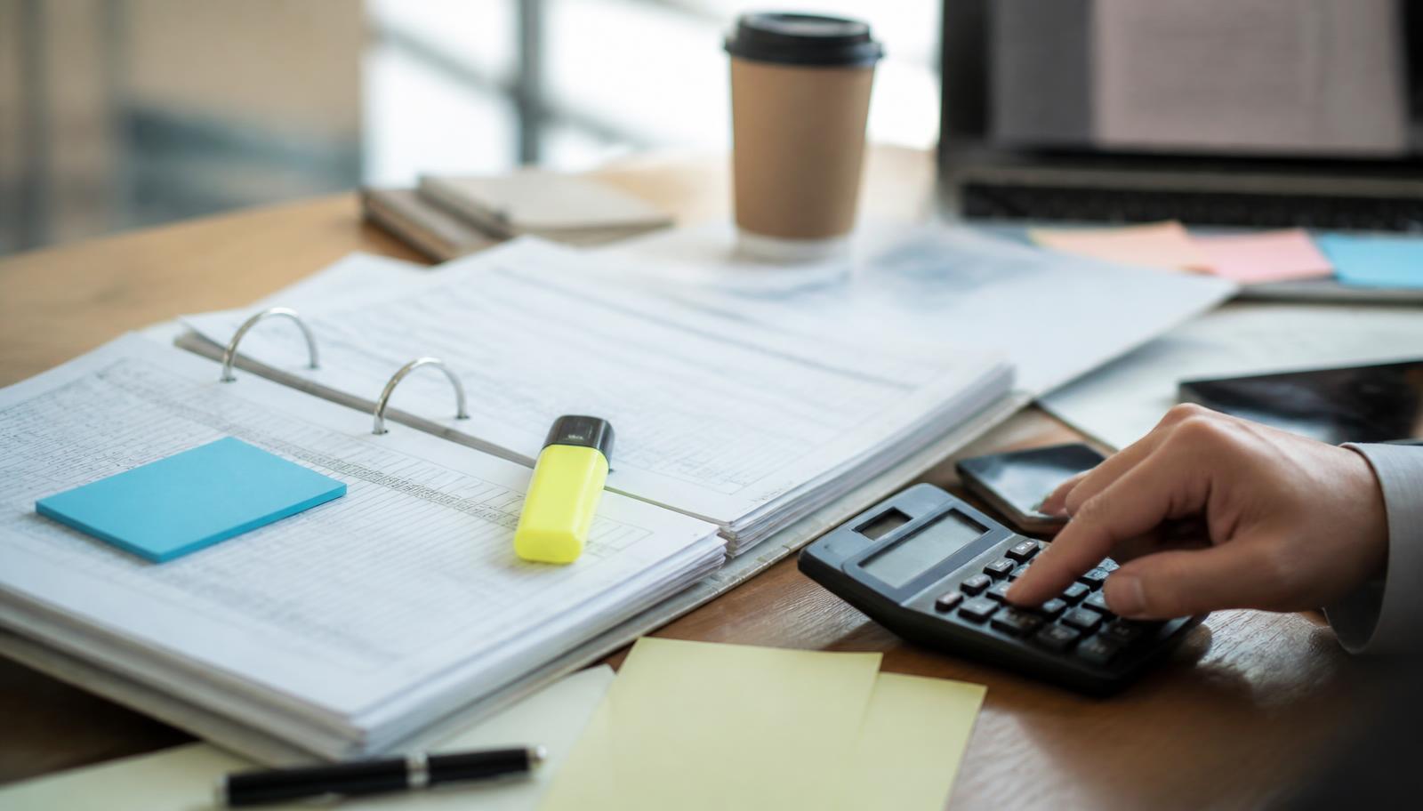 Pasta com relatórios financeiros impressos, marca-texto e calculadora sobre mesa de trabalho